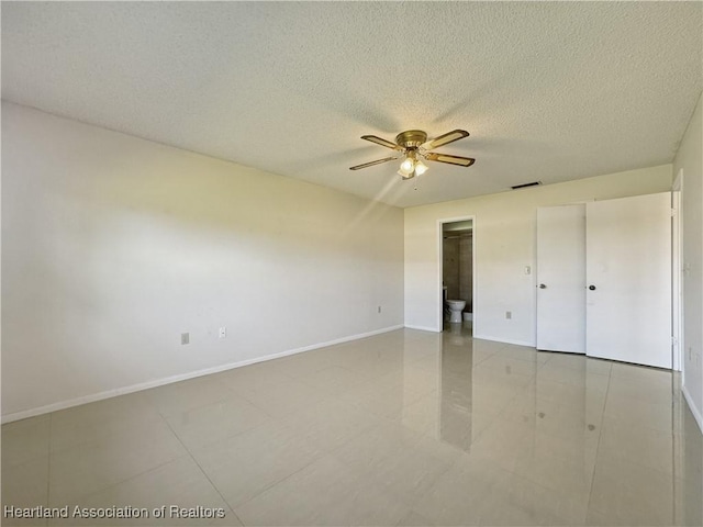 unfurnished bedroom with ensuite bath, ceiling fan, light tile patterned floors, and a textured ceiling