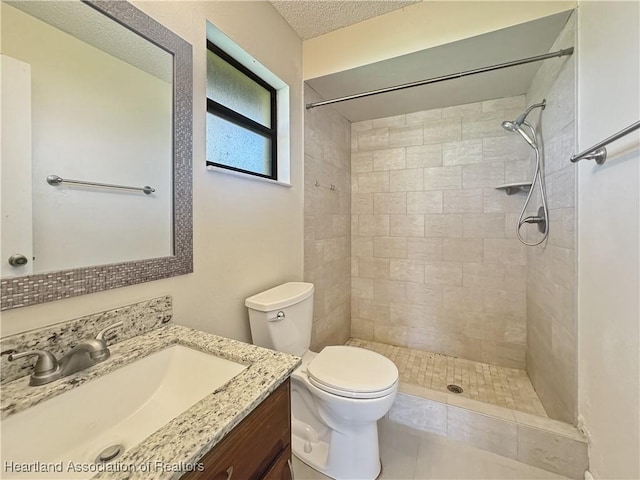 bathroom with vanity, toilet, tiled shower, and a textured ceiling