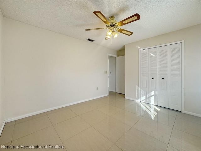 unfurnished bedroom with ceiling fan, a closet, light tile patterned floors, and a textured ceiling