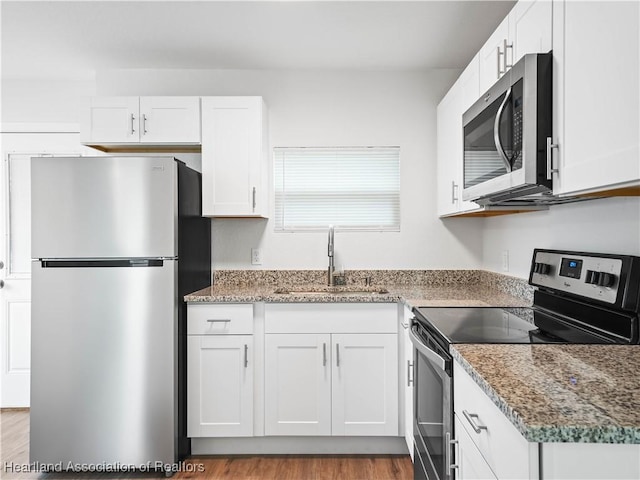 kitchen featuring white cabinets, stainless steel appliances, a sink, and wood finished floors