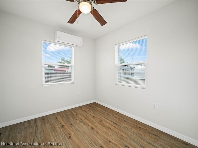 empty room featuring baseboards, a wall unit AC, wood finished floors, and a wealth of natural light
