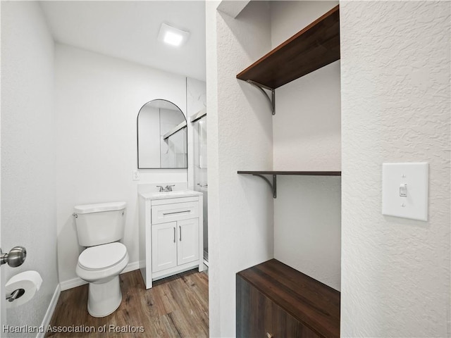 bathroom with a shower, wood finished floors, vanity, toilet, and a textured wall