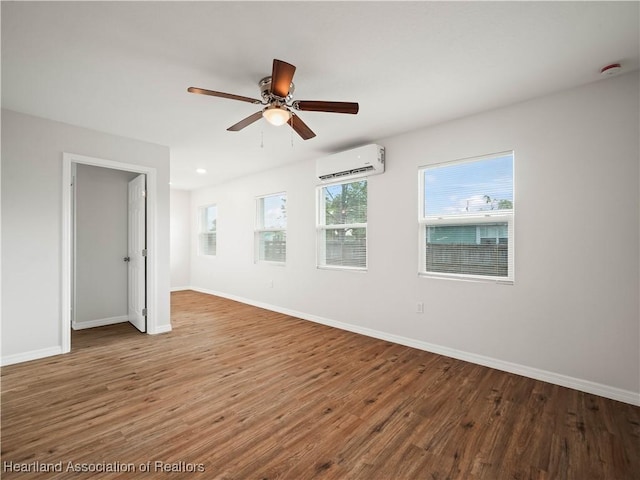 spare room with baseboards, an AC wall unit, and wood finished floors