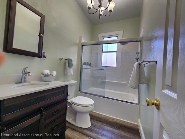 bathroom with toilet, an inviting chandelier, wood finished floors, enclosed tub / shower combo, and vanity