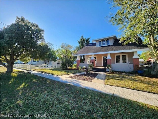 bungalow featuring brick siding, covered porch, a front yard, and fence