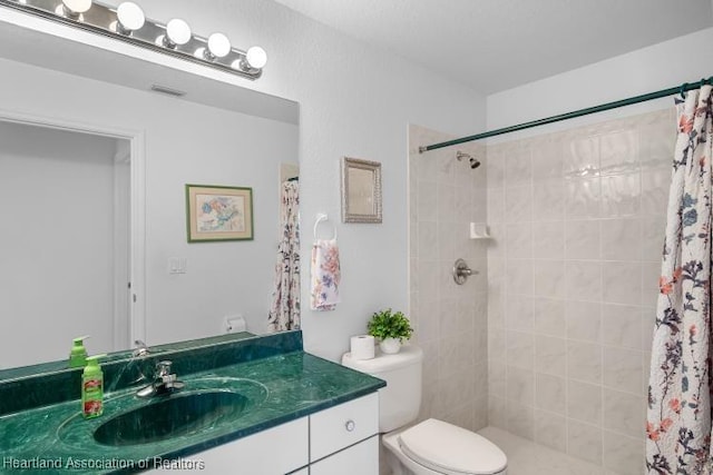 bathroom with toilet, a tile shower, visible vents, and vanity