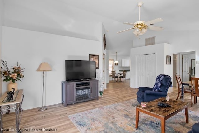living room with light wood finished floors, a ceiling fan, high vaulted ceiling, and baseboards