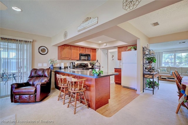 kitchen with kitchen peninsula, light colored carpet, electric stove, white refrigerator, and a breakfast bar area