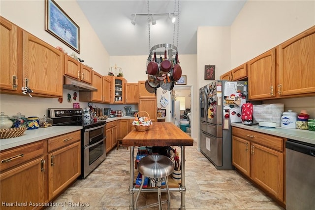 kitchen featuring glass insert cabinets, stone finish floor, light countertops, under cabinet range hood, and appliances with stainless steel finishes