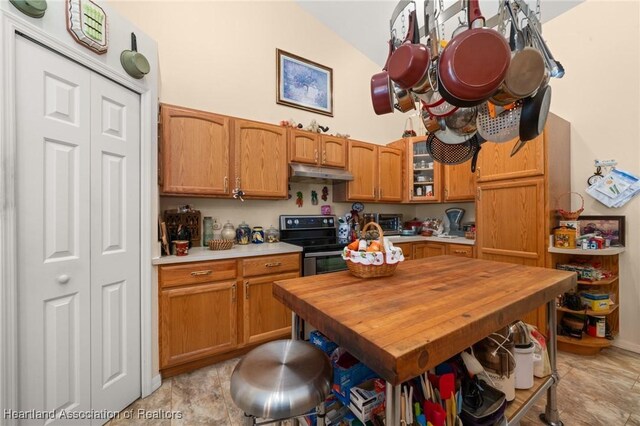kitchen with high vaulted ceiling, electric stove, brown cabinetry, light countertops, and under cabinet range hood