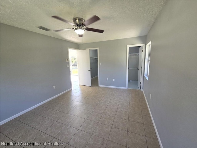 empty room with ceiling fan, a healthy amount of sunlight, light tile patterned floors, and a textured ceiling