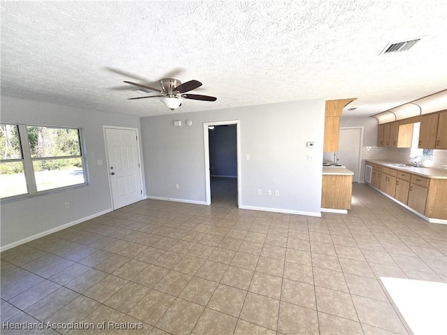 unfurnished living room featuring a textured ceiling, ceiling fan, light tile patterned flooring, and sink