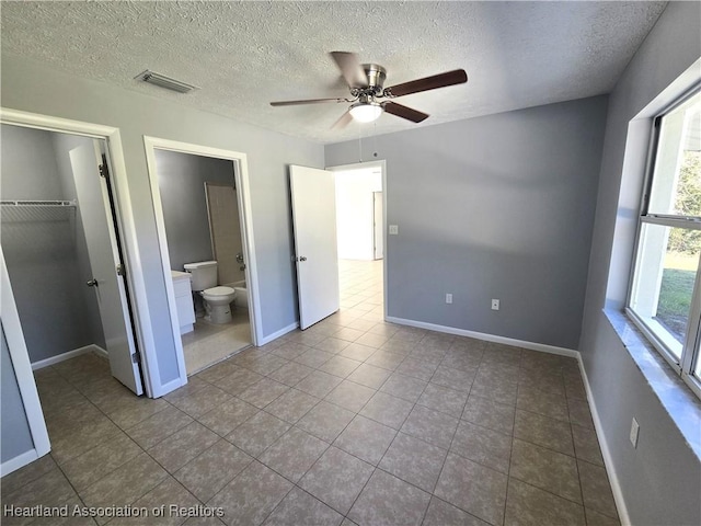 unfurnished bedroom featuring ensuite bathroom, ceiling fan, light tile patterned floors, a spacious closet, and a closet