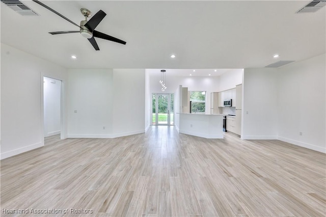 unfurnished living room with ceiling fan with notable chandelier and light wood-type flooring