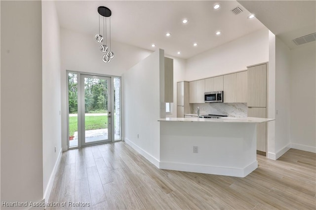 kitchen with kitchen peninsula, light hardwood / wood-style flooring, a towering ceiling, and pendant lighting