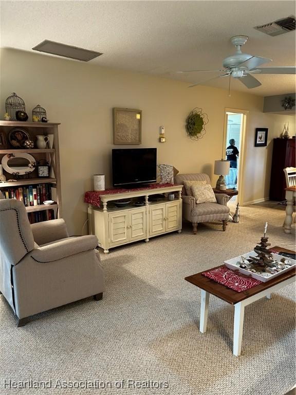 living area featuring a ceiling fan, visible vents, and light colored carpet