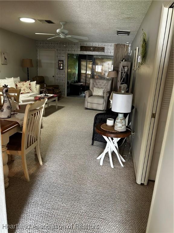 carpeted dining room featuring a textured ceiling, a ceiling fan, visible vents, and wallpapered walls