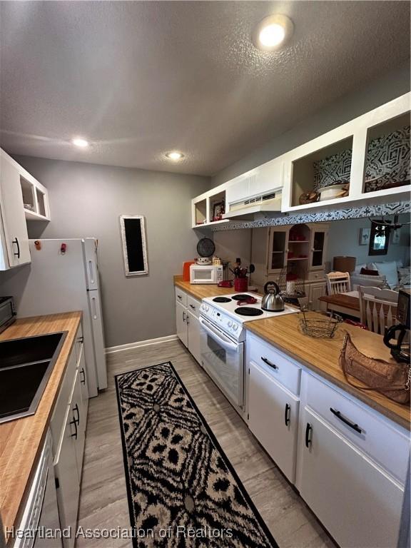 kitchen with white appliances, white cabinetry, wood counters, and open shelves