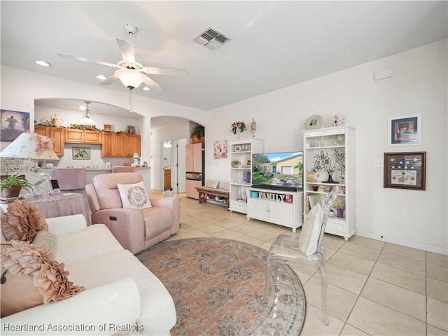 living area featuring arched walkways, light tile patterned floors, visible vents, baseboards, and a ceiling fan