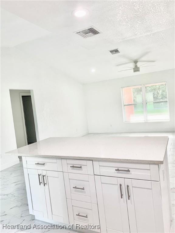 kitchen featuring a textured ceiling, white cabinetry, and ceiling fan