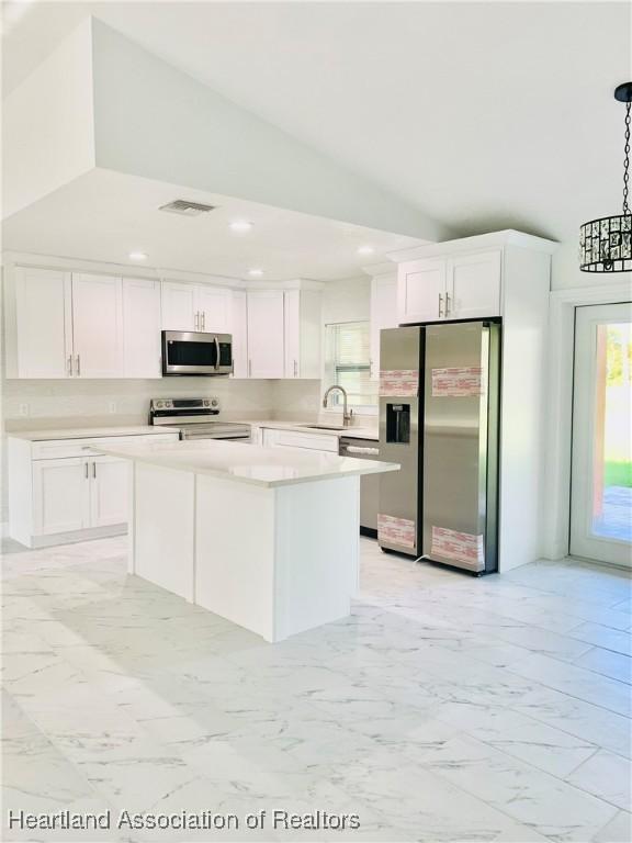 kitchen with appliances with stainless steel finishes, sink, pendant lighting, white cabinets, and a center island