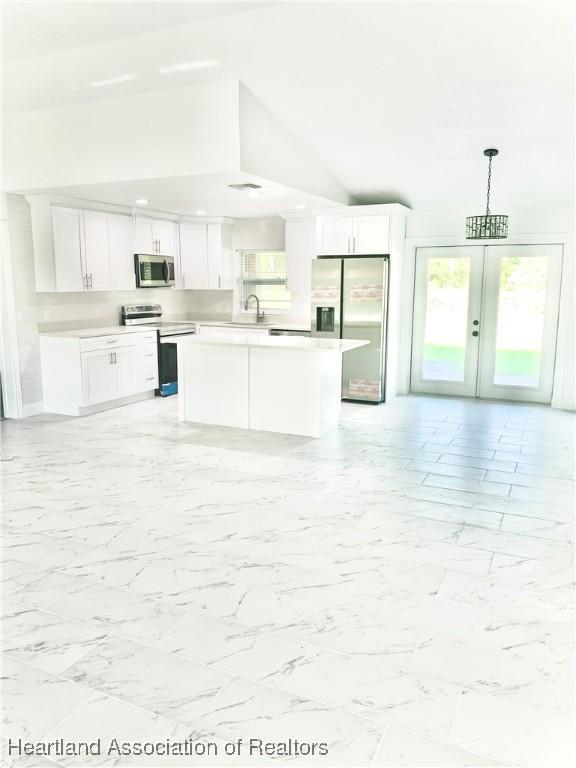 kitchen with stainless steel appliances, sink, decorative light fixtures, white cabinets, and lofted ceiling