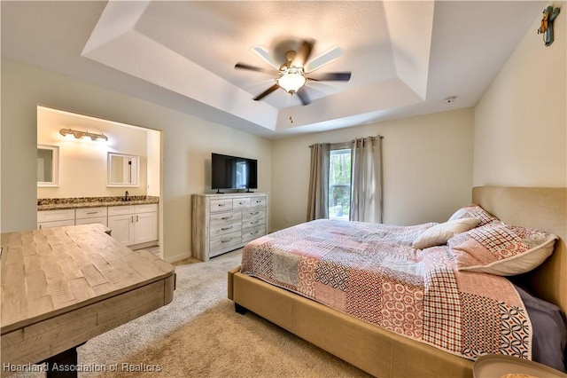 bedroom featuring sink, ensuite bathroom, ceiling fan, a raised ceiling, and light carpet