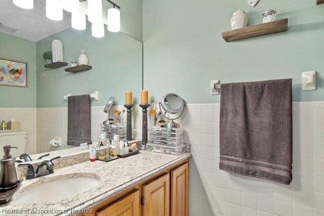 bathroom featuring visible vents, toilet, vanity, and tile walls