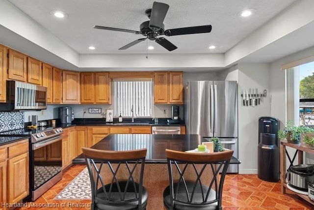 kitchen with appliances with stainless steel finishes, brown cabinetry, dark countertops, and a sink