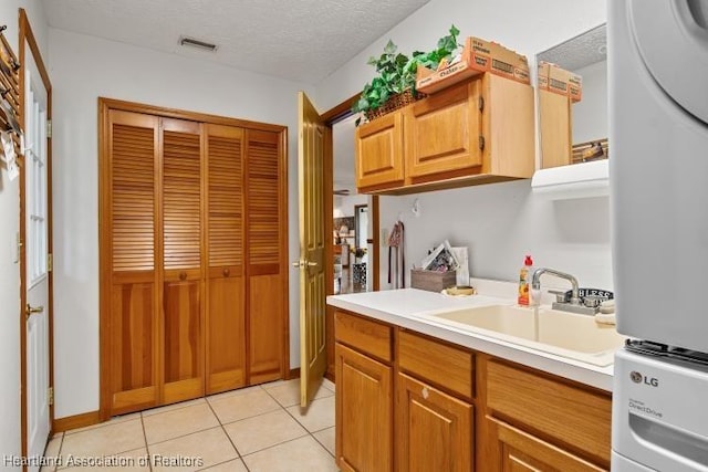 kitchen with light countertops, a sink, visible vents, and stacked washer / drying machine