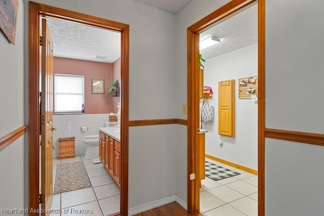 hall with a textured ceiling, light tile patterned floors, wainscoting, and tile walls