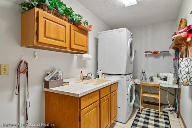 washroom with stacked washer and dryer, cabinet space, a textured ceiling, a sink, and light tile patterned flooring