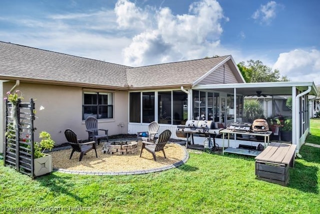 rear view of house featuring a fire pit, a sunroom, roof with shingles, a yard, and stucco siding