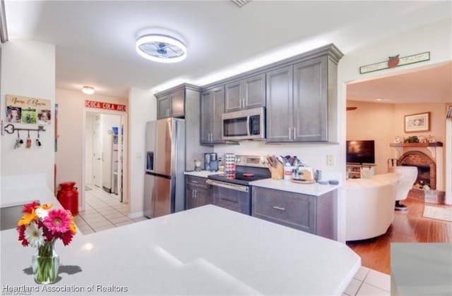 kitchen featuring gray cabinetry, light tile patterned flooring, stainless steel appliances, and a brick fireplace