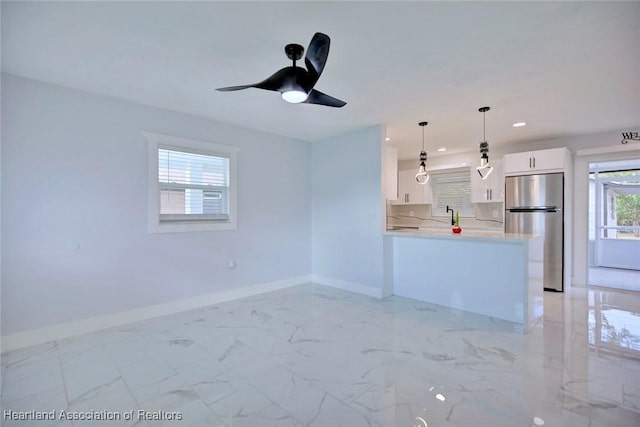 kitchen with kitchen peninsula, stainless steel fridge, a healthy amount of sunlight, decorative light fixtures, and white cabinets