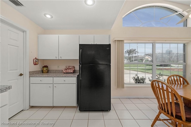 kitchen with black refrigerator, white cabinets, vaulted ceiling, and light tile patterned flooring