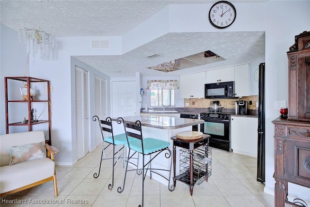 kitchen with a textured ceiling, black appliances, a breakfast bar, and white cabinets