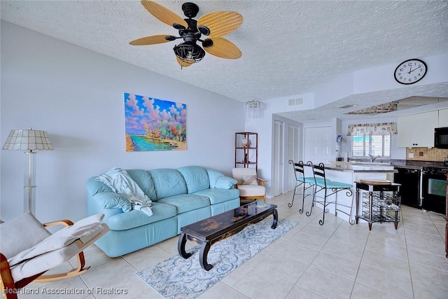 living room featuring ceiling fan, sink, a textured ceiling, and light tile patterned floors