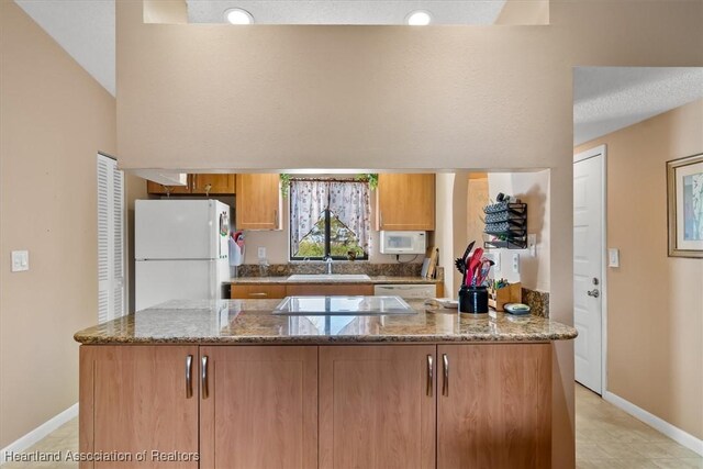 kitchen featuring kitchen peninsula, white appliances, stone countertops, and sink