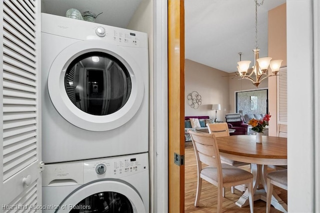 laundry area with hardwood / wood-style flooring, an inviting chandelier, and stacked washer / dryer