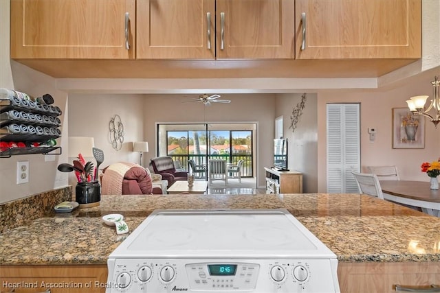 kitchen featuring light stone countertops, stove, and ceiling fan with notable chandelier