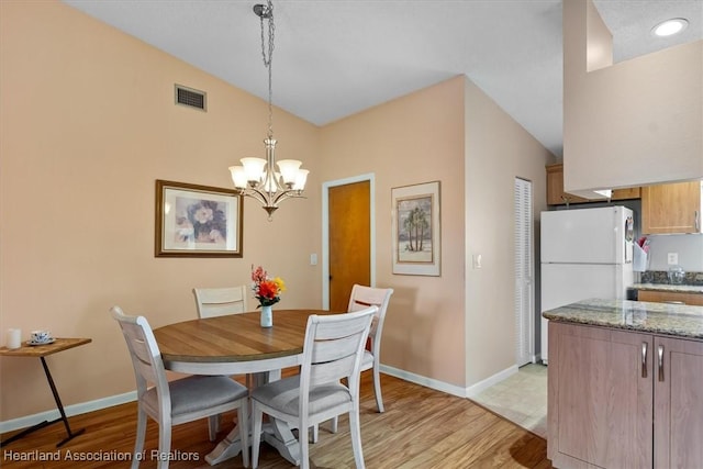 dining area featuring a notable chandelier, light hardwood / wood-style floors, and vaulted ceiling