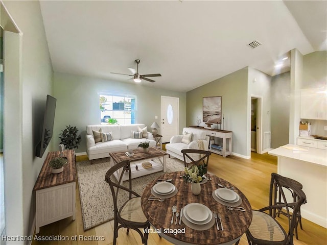 living area featuring a ceiling fan, baseboards, visible vents, vaulted ceiling, and light wood-type flooring