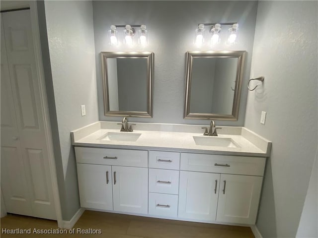 full bath with double vanity, baseboards, a textured wall, and a sink