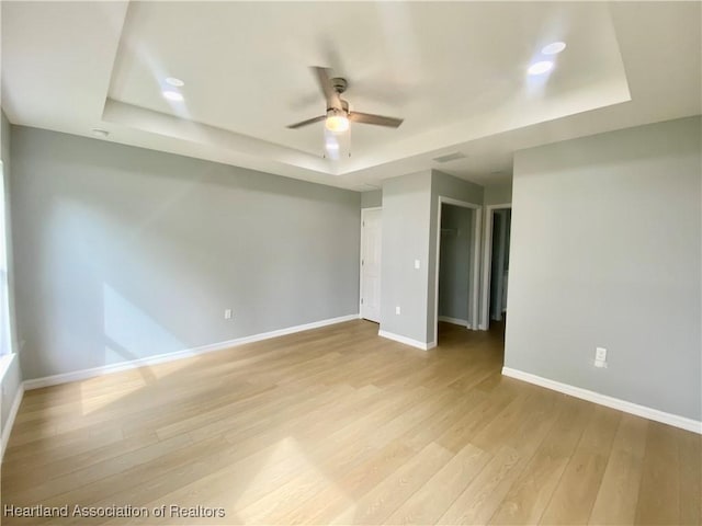 unfurnished room featuring light wood finished floors, visible vents, ceiling fan, baseboards, and a raised ceiling