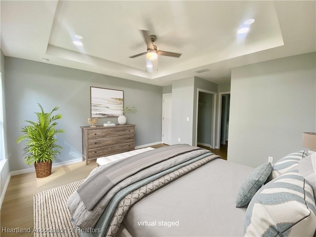 bedroom with a tray ceiling, wood finished floors, and baseboards