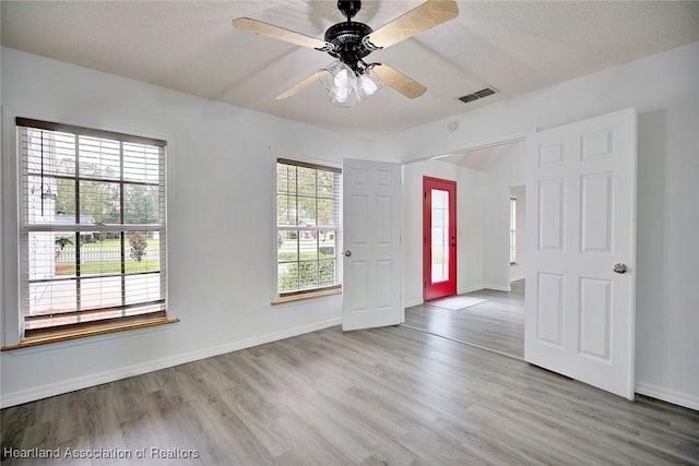 unfurnished room featuring ceiling fan, a healthy amount of sunlight, light hardwood / wood-style floors, and a textured ceiling