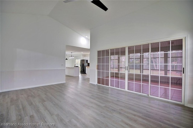 empty room with hardwood / wood-style floors, ceiling fan with notable chandelier, and lofted ceiling