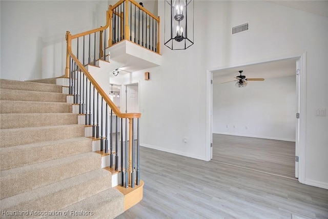 stairway featuring hardwood / wood-style floors, a towering ceiling, and ceiling fan with notable chandelier