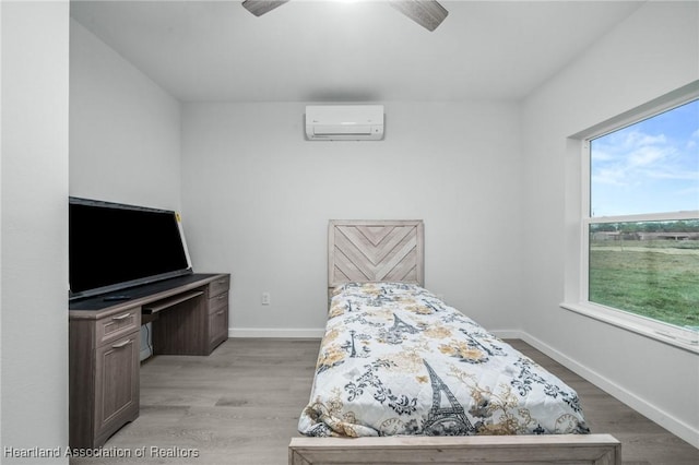 bedroom with light wood-type flooring, ceiling fan, and a wall mounted air conditioner